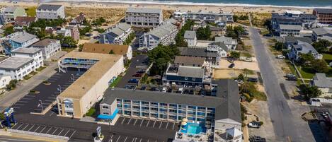 An aerial view of a coastal hotel with multiple buildings, a parking lot, and a beach in the background.