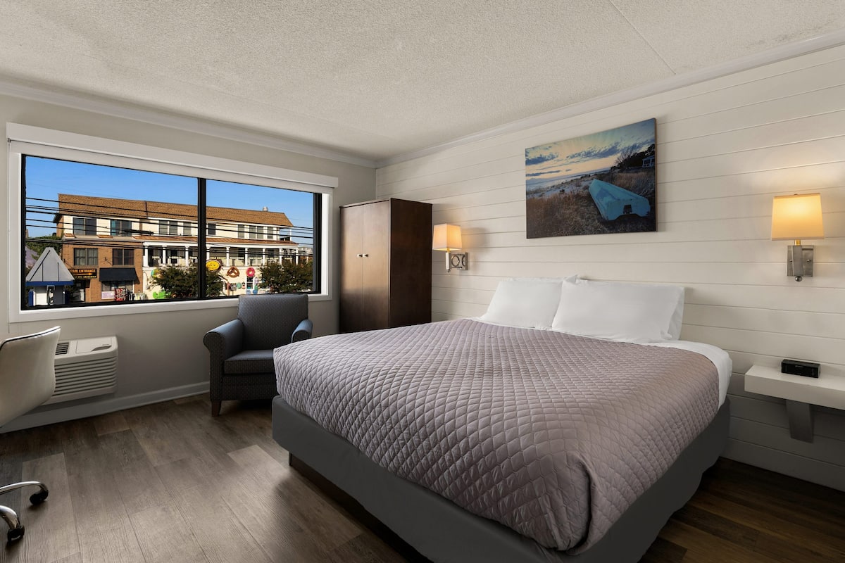 A modern hotel room with a large bed, a desk, a chair, and a window with a view of the city.