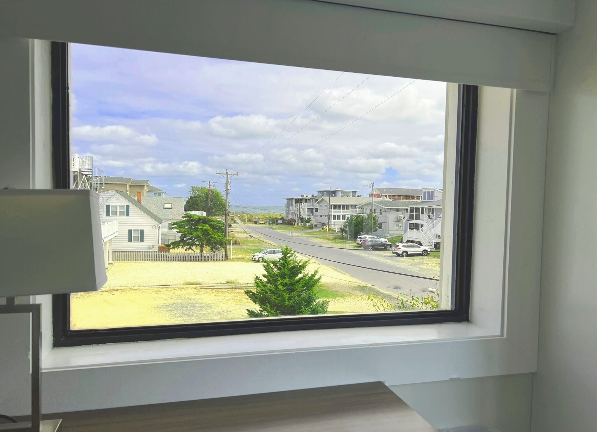 A window with a view of a residential street, houses, and parked cars.