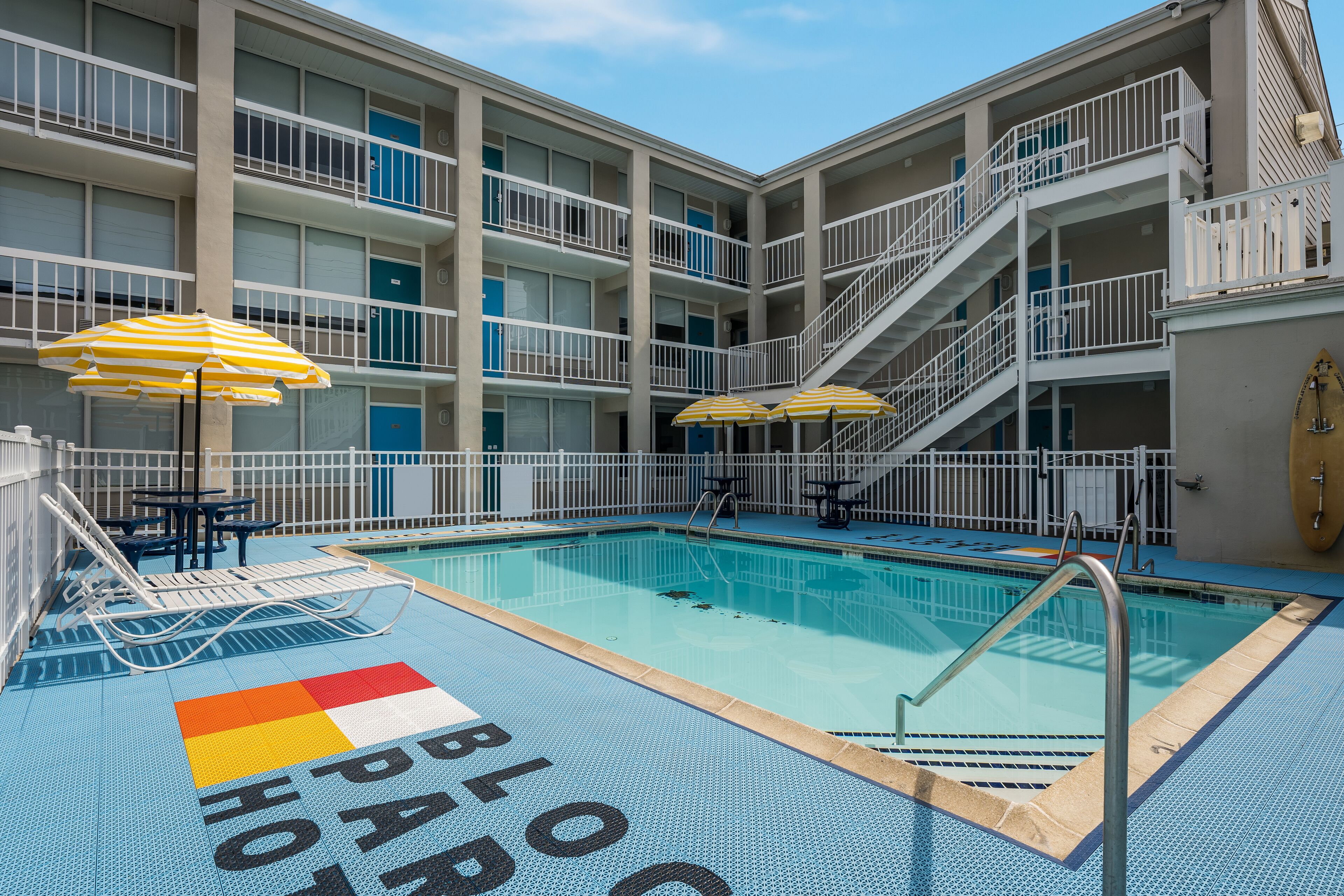 A swimming pool with a blue deck, surrounded by a multi-story building with balconies and stairs.
