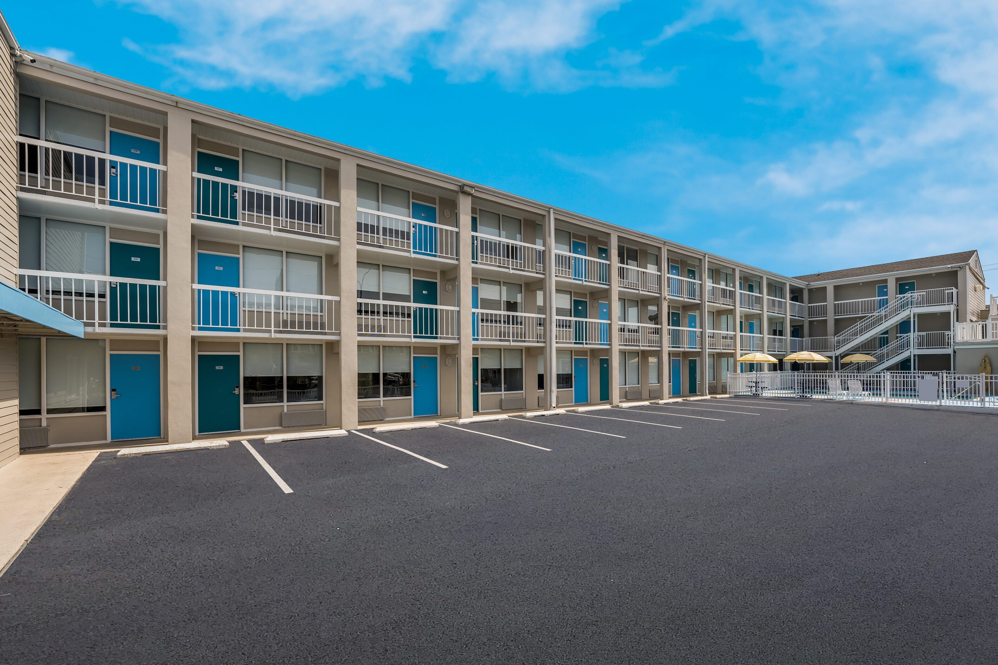 A multi-story motel with a central courtyard, individual rooms with balconies, and a staircase leading to an upper level.