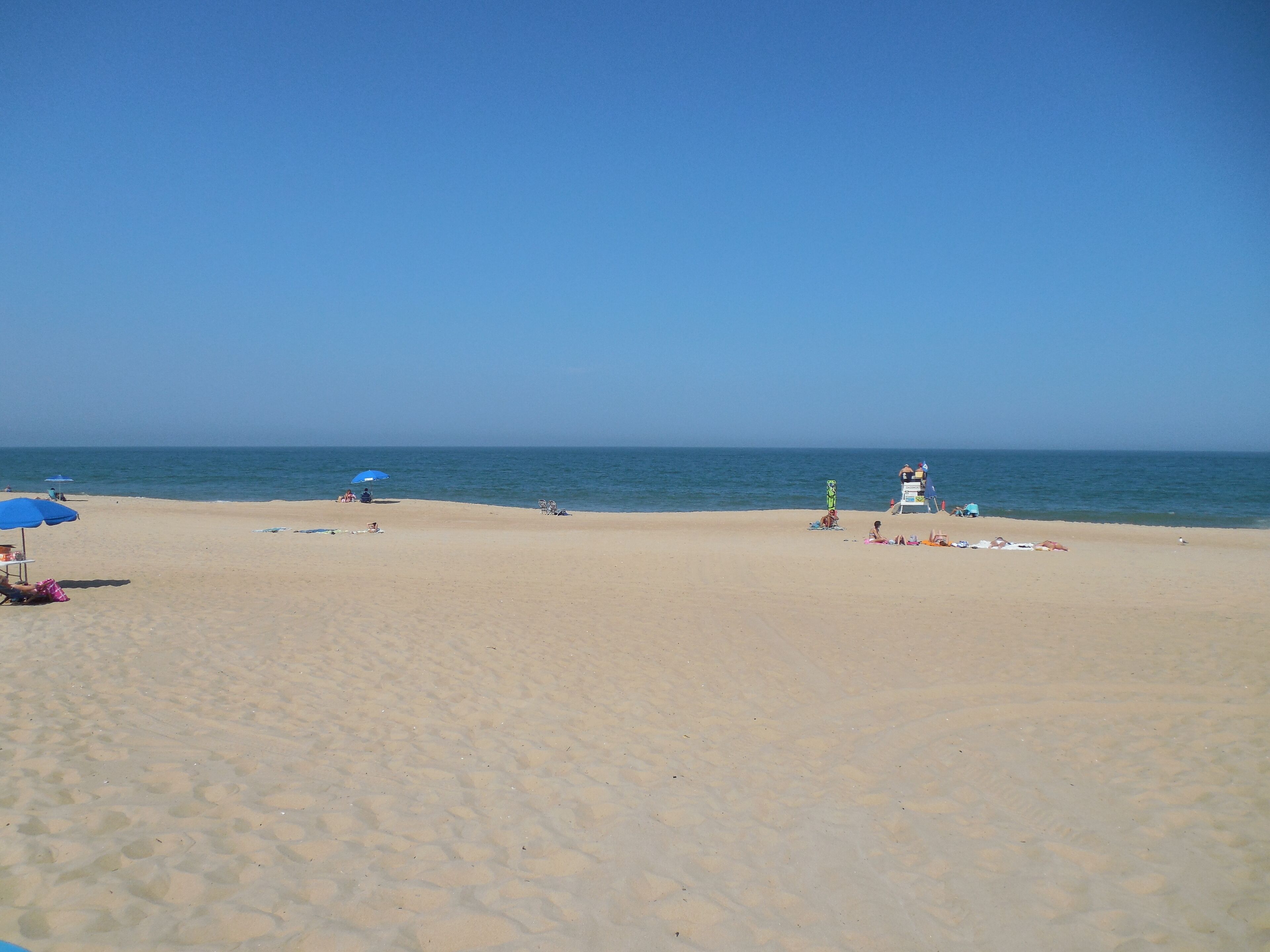 A beach with a lifeguard tower, umbrellas, and beach chairs.