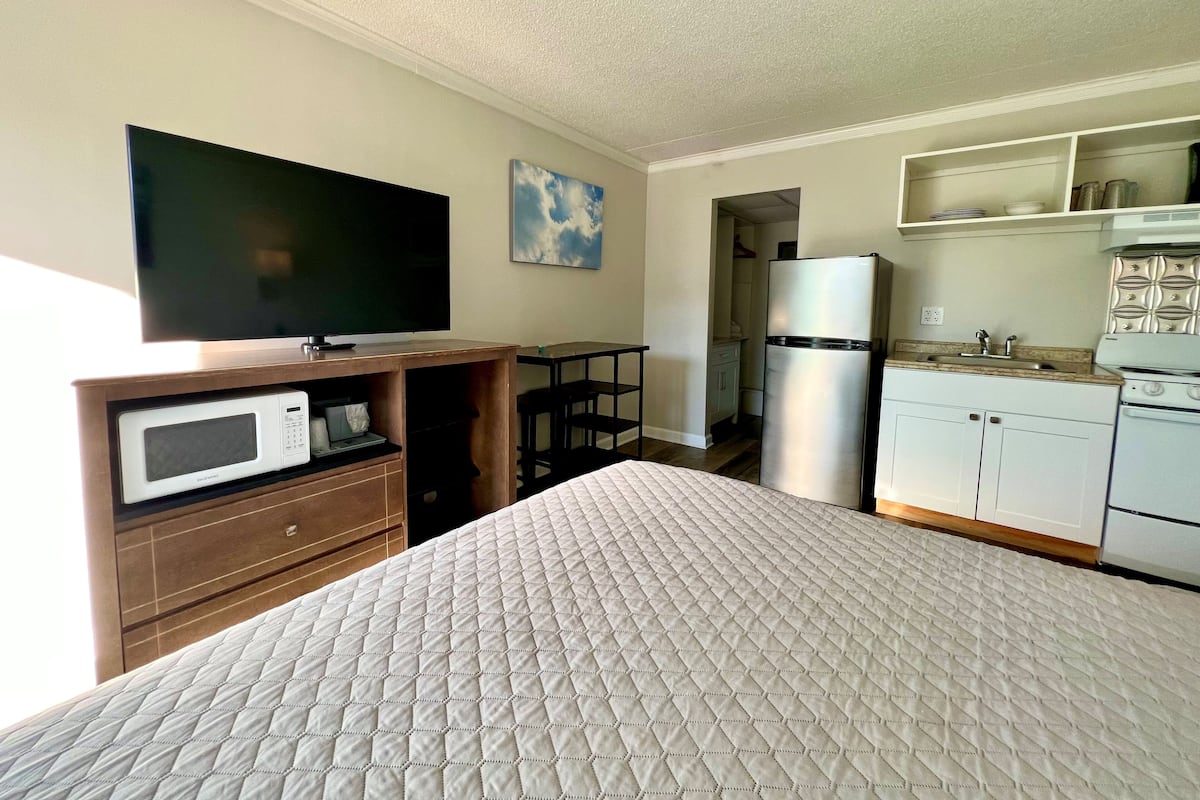 A compact hotel room with a bed, a TV, a microwave, a refrigerator, and a kitchenette.