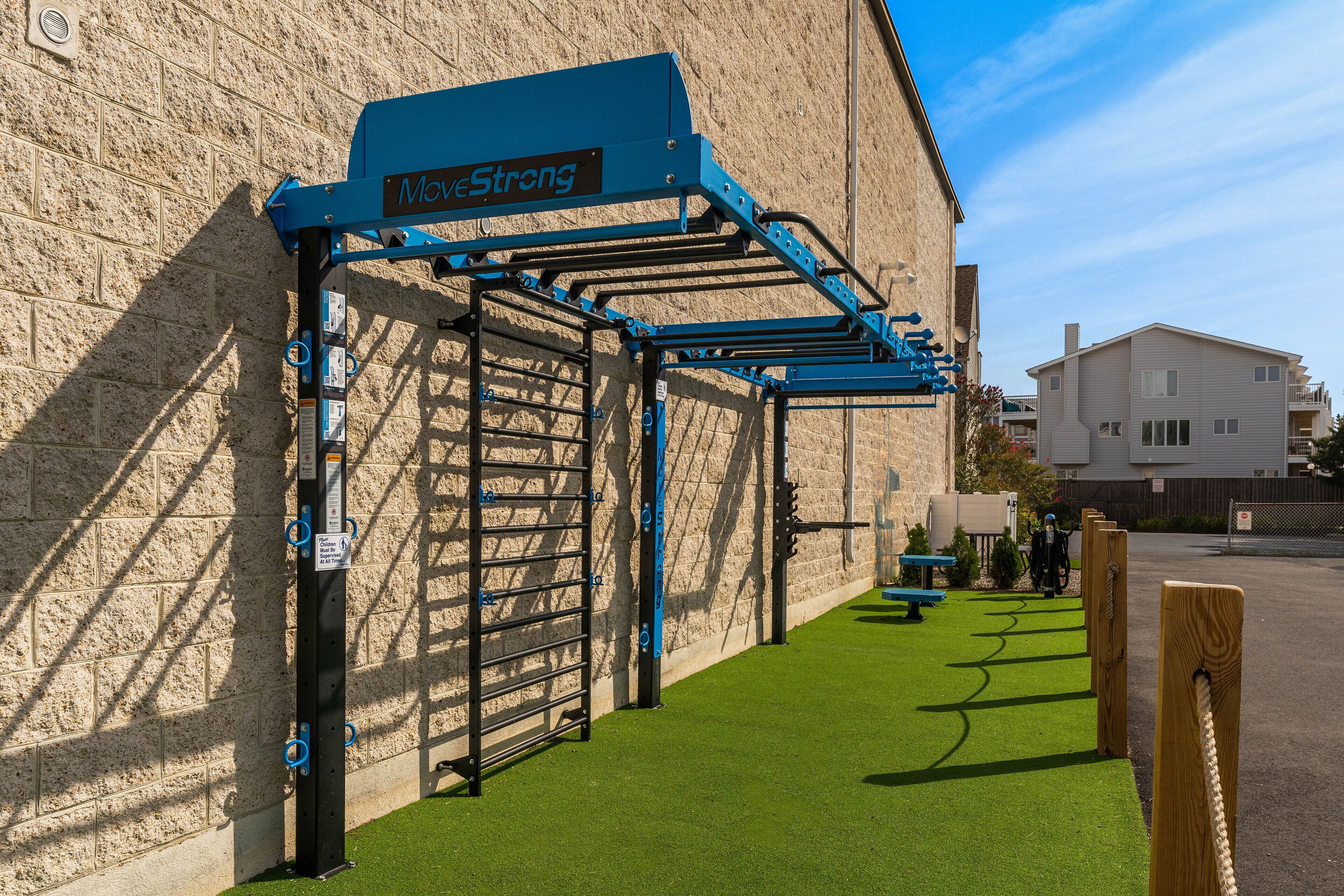 A gym with outdoor exercise equipment, a wall-mounted sign, and a green artificial turf area.