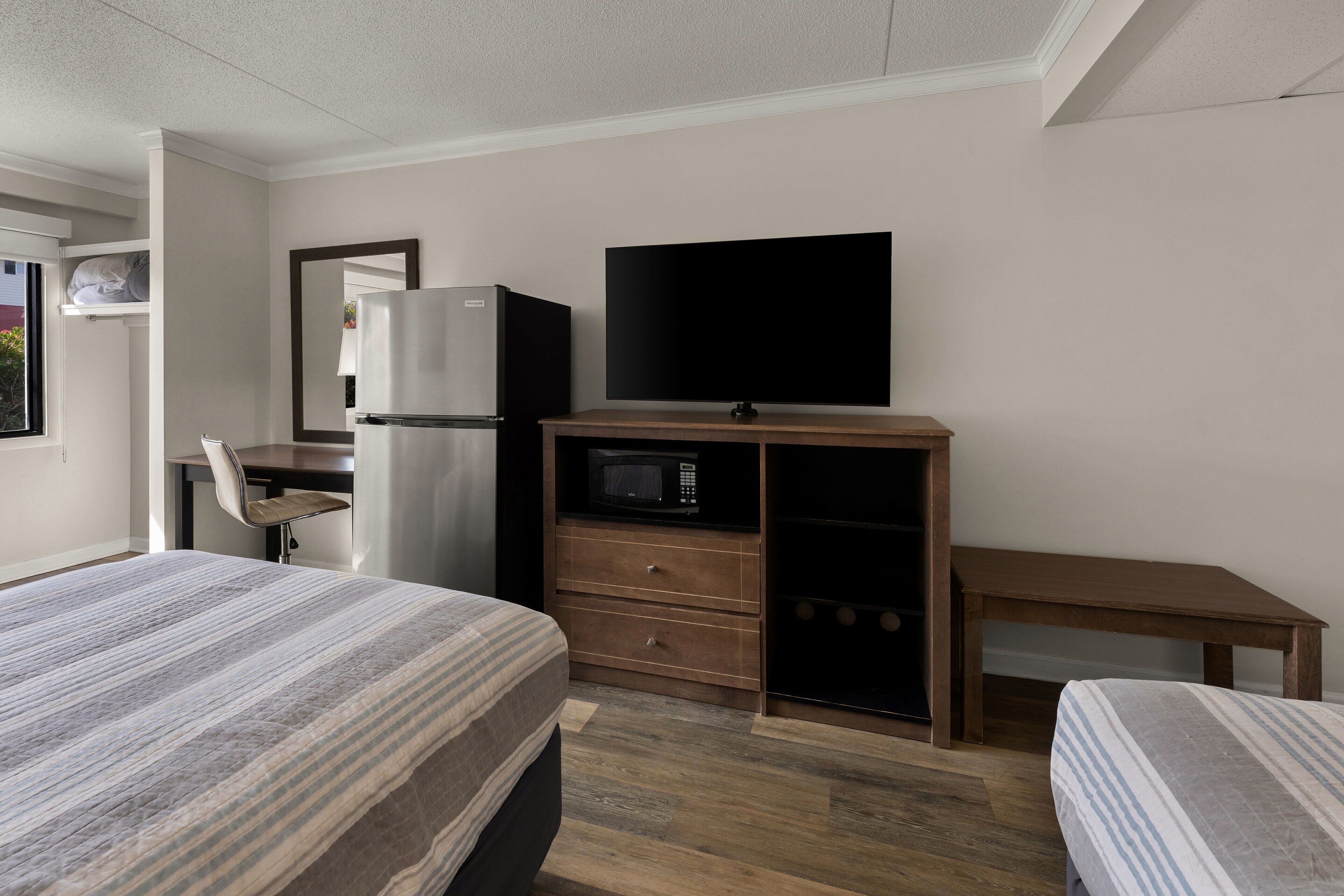 A hotel room with a bed, a desk, a refrigerator, a microwave, and a television.
