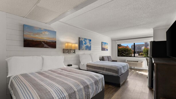 A hotel room with two beds, a TV, a window with a city view, and artwork on the walls. - Atlantic Oceanside Dewey (Dewey Beach)