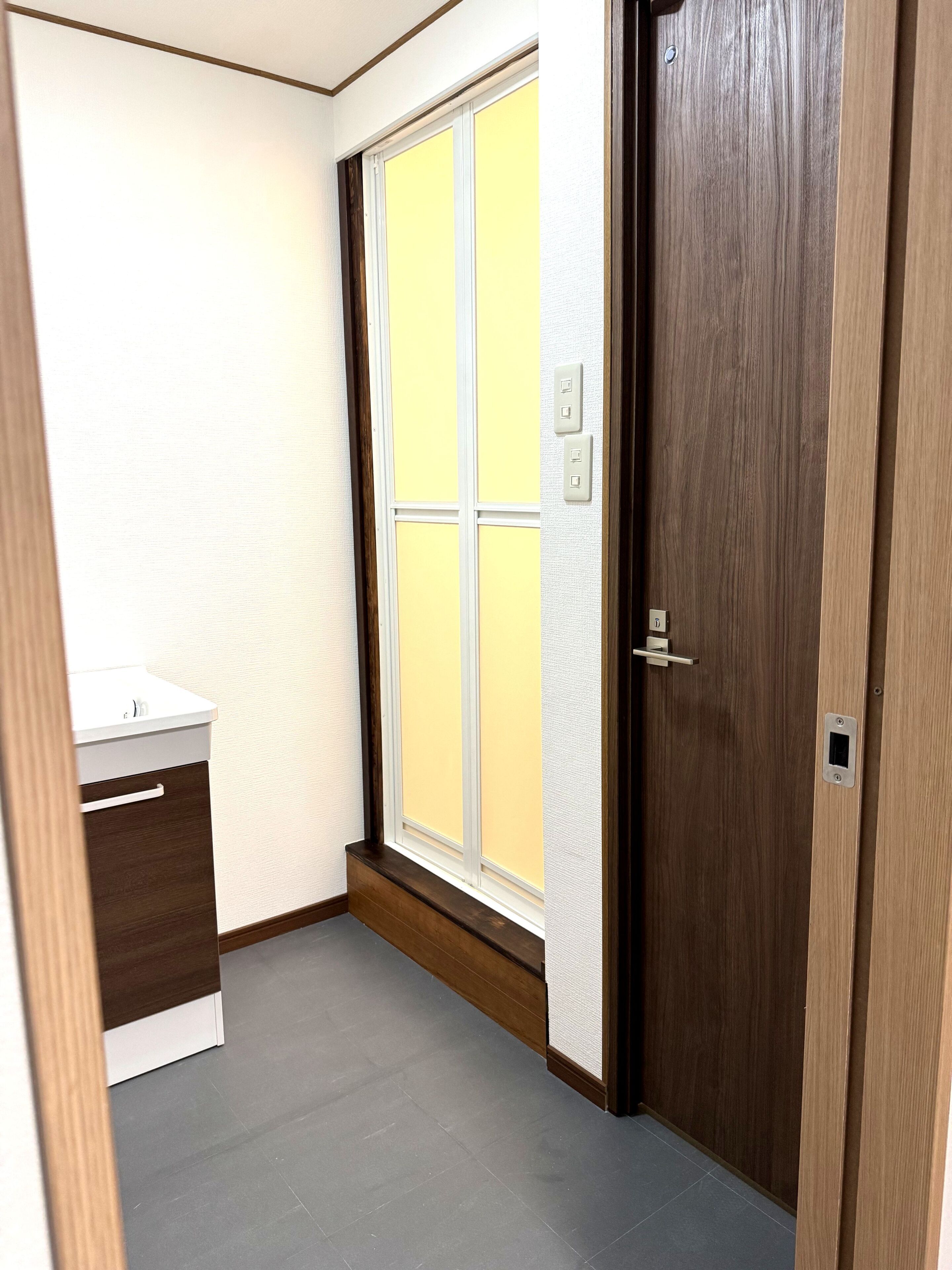 A room with a wooden door, a window with a view, a white sink, and a tiled floor.