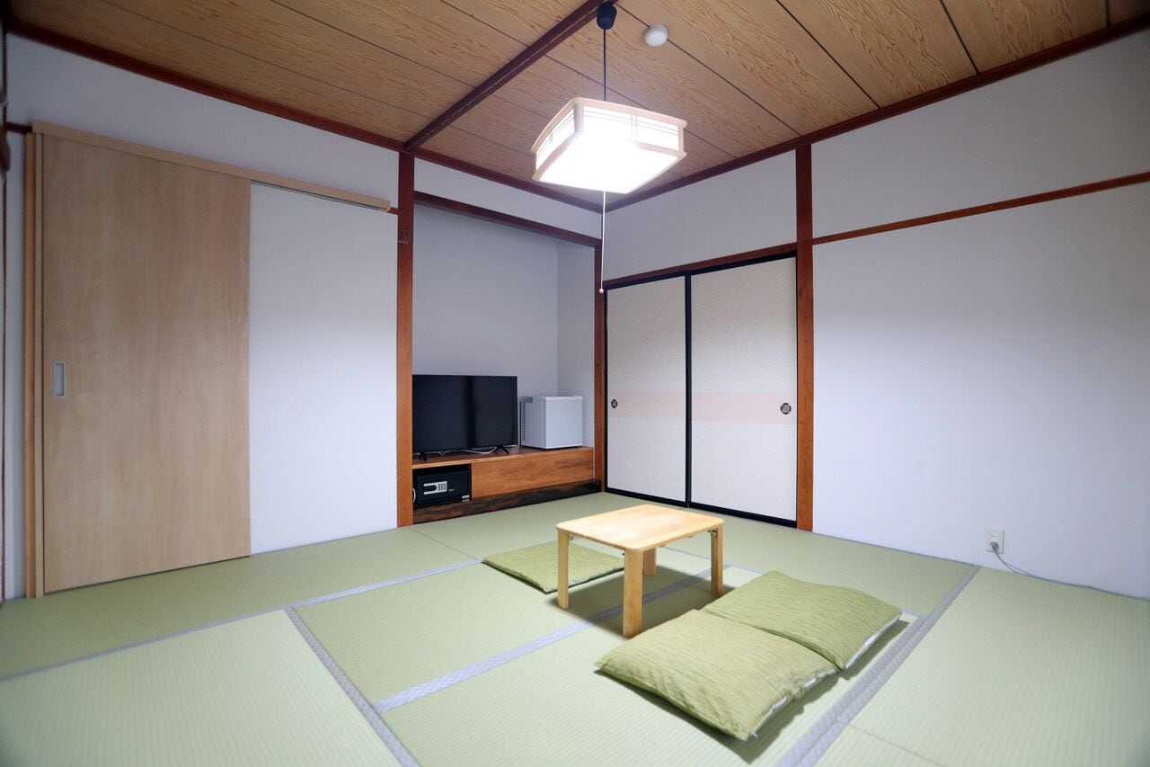 A traditional Japanese room with tatami flooring, a low wooden table, a television, and sliding doors.