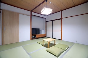 Una habitación tradicional japonesa con suelo de tatami, una mesa de madera baja, un televisor y puertas correderas.