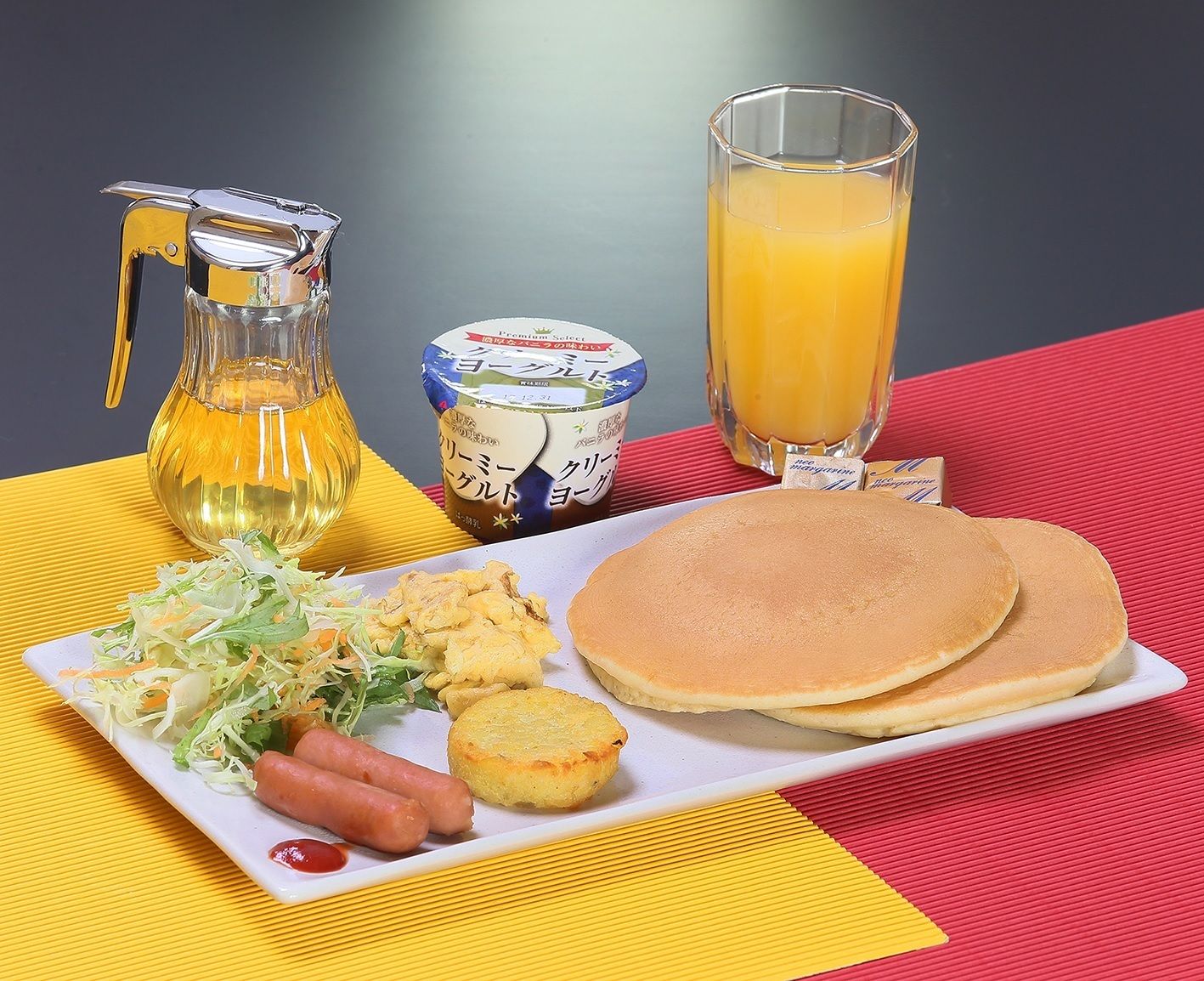 Un plato de desayuno con panqueques, salchichas, ensalada de col y una jarra de jugo.