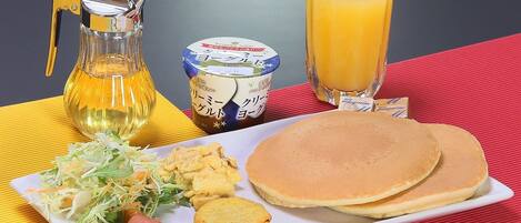 Un plato de desayuno con panqueques, salchichas, ensalada de col y una jarra de jugo.