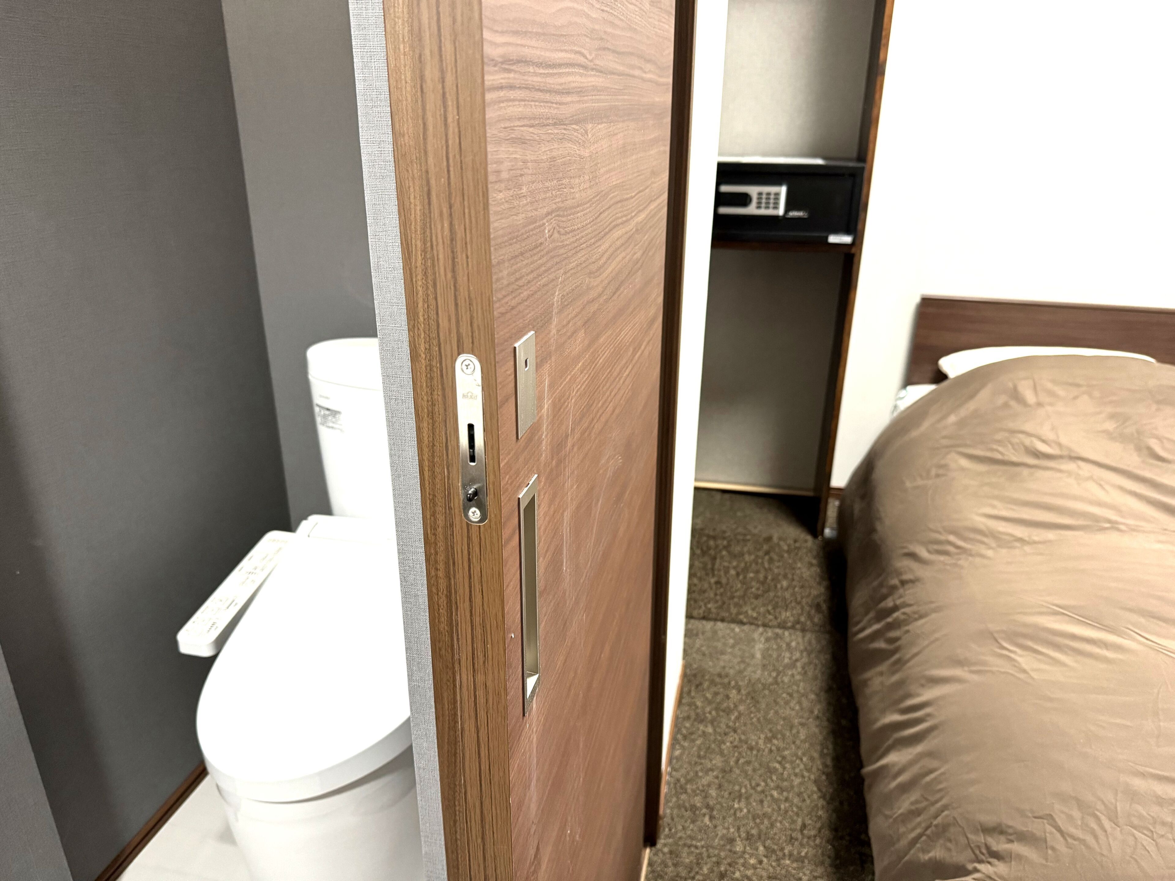 A bathroom with a toilet, a wooden door with a handle, and a bed with a mattress.