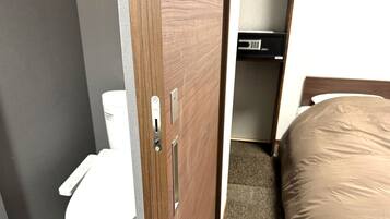 A bathroom with a toilet, a wooden door with a handle, and a bed with a mattress.