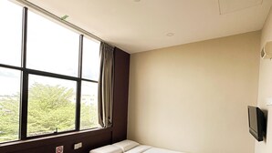 Habitación de hotel con dos camas, un ventanal grande, televisión y vistas al exterior con vegetación.
