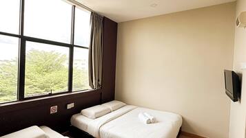 A hotel room with two beds, a large window, a TV, and a view of greenery outside.
