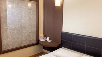 A hotel room with a bed, a nightstand, a wall-mounted air conditioner, a marble-patterned wall, and a wall-mounted light.