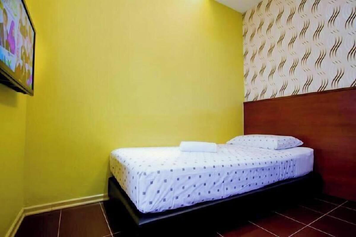 A single bed with a patterned bedspread, a wooden headboard, and a wall with a wavy pattern.