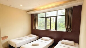 Una habitación de hotel con tres camas individuales, un ventanal grande con cortinas y un cabecero de madera.