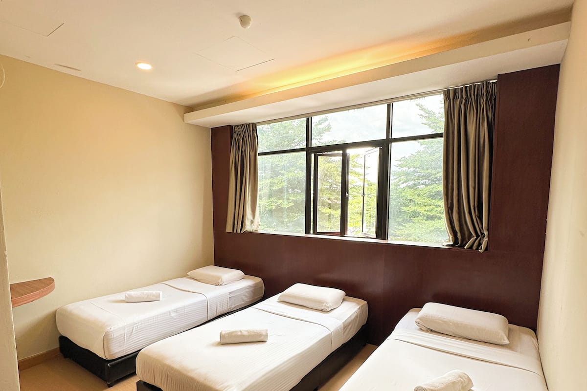A hotel room with three single beds, a large window with curtains, and a wooden headboard.
