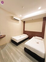 Habitación de hotel con dos camas, cabecero de madera, aire acondicionado de pared y suelo de madera.