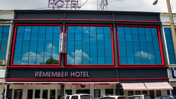 Un hotel con un letrero grande que dice "Remember Hotel" y varias ventanas. Varias coches estacionados adelante.