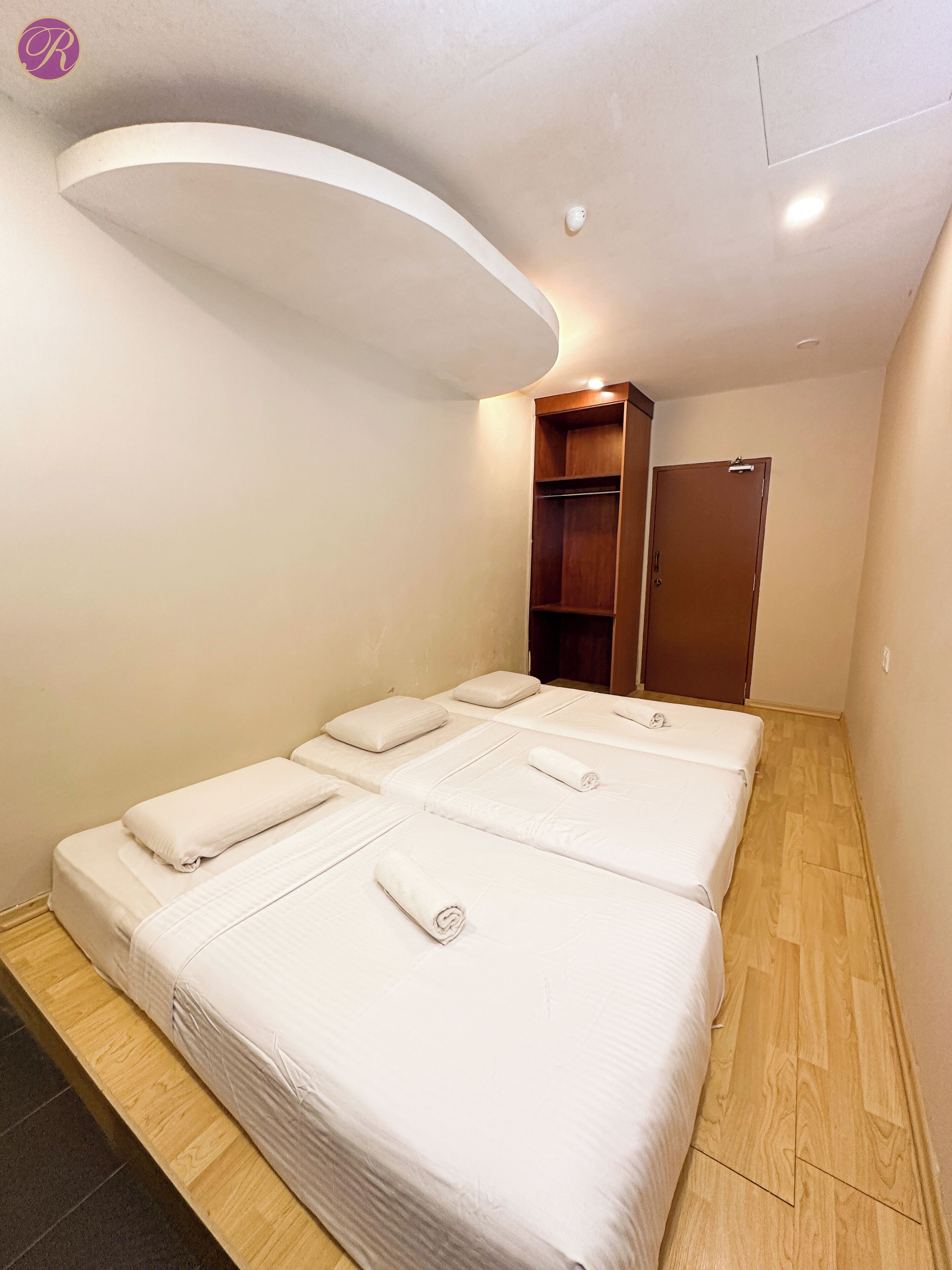 Quarto de hotel com três camas, um guarda-roupa de madeira e uma luminária no teto.