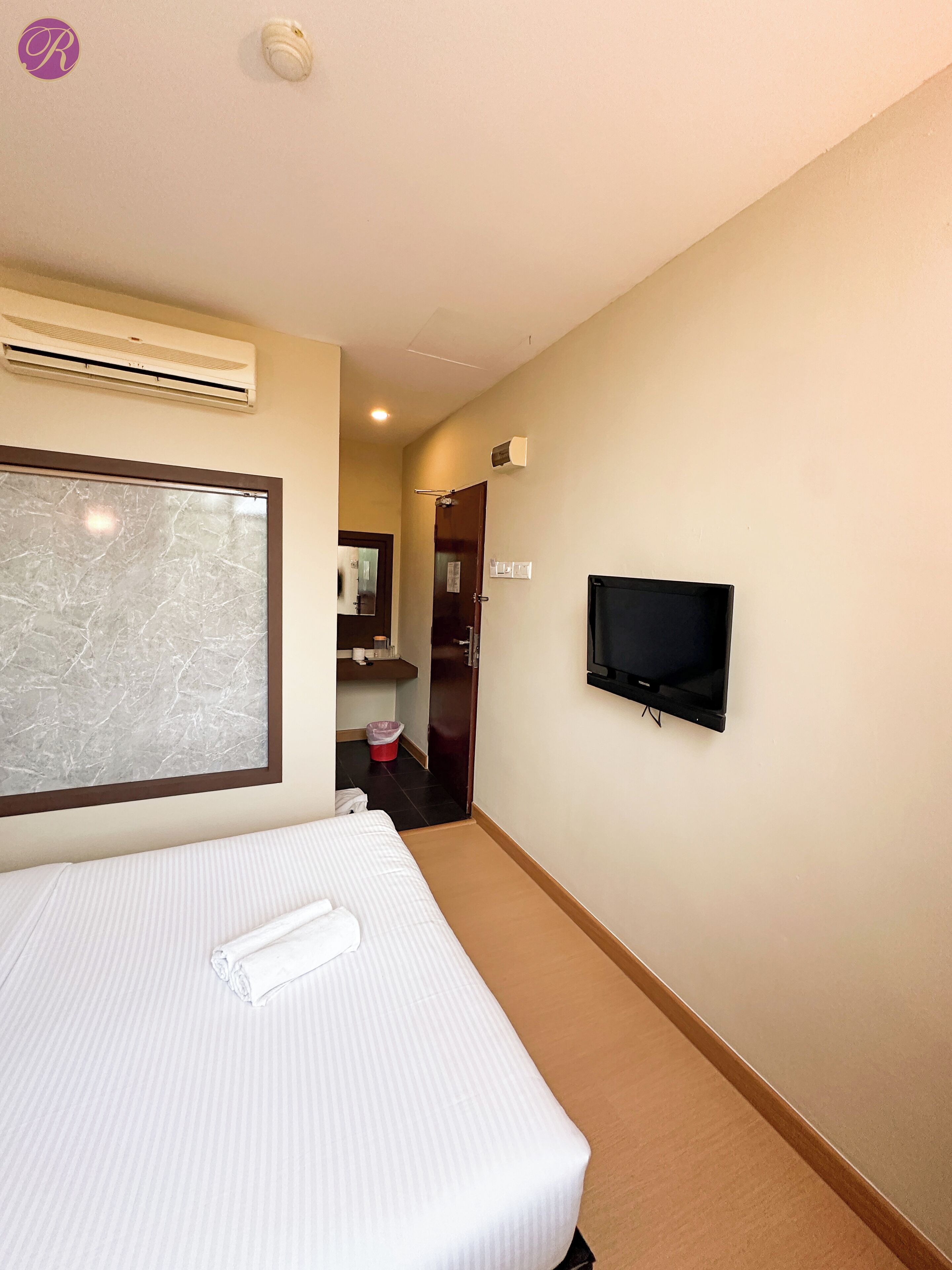 A hotel room with a bed, a TV mounted on the wall, an air conditioning unit, and a marble-patterned window.