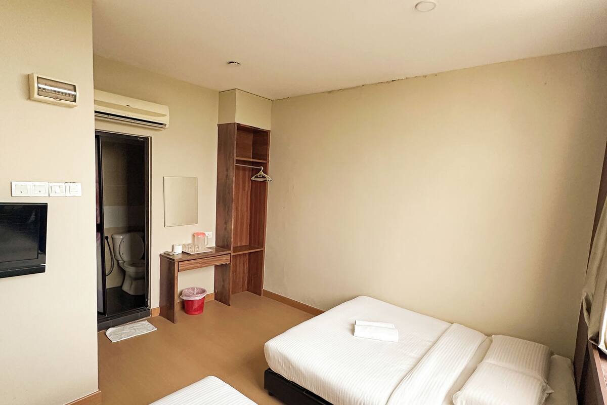 A hotel room with two beds, a wardrobe, a mirror, and a small table with a red bucket.