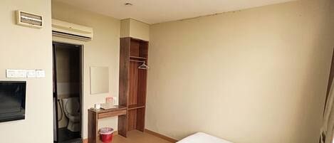 Habitación de hotel con dos camas, un armario, un espejo y una pequeña mesa con un cubo rojo.