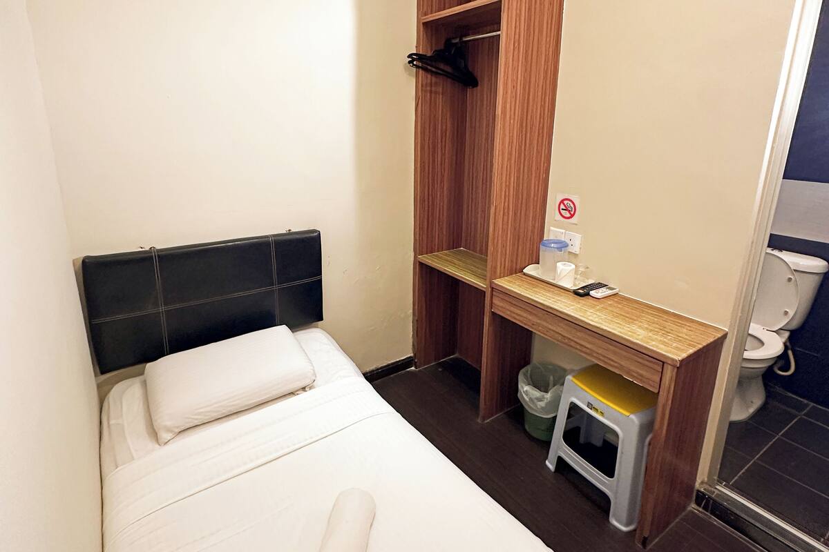A small, compact room with a bed, a wooden desk, and a toilet.