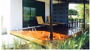 A modern outdoor patio with a wooden deck, two wooden chairs, and a glass door leading to a garden. - Wanlapa Farmstay (Lop Buri)