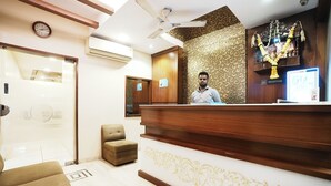 A reception area with a wooden reception desk, a clock, and a ceiling fan. - Hotel Airport Metro (Mumbai)
