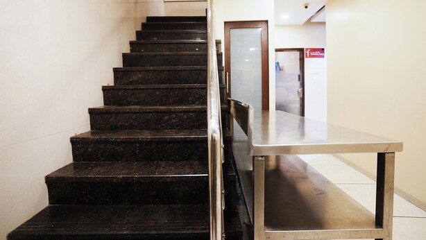 A staircase with a metal handrail leading to a room with a large metal table. - Hotel Airport Metro (Mumbai)