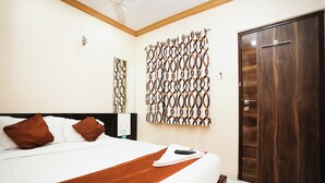 A hotel room with a large bed, a wooden headboard, a brown throw blanket, and a wooden wardrobe. - Hotel Airport Metro (Mumbai)