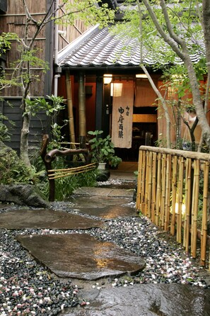 Un jardín japonés tradicional con un sendero de piedra que lleva a un edificio de madera con techo de tejas.