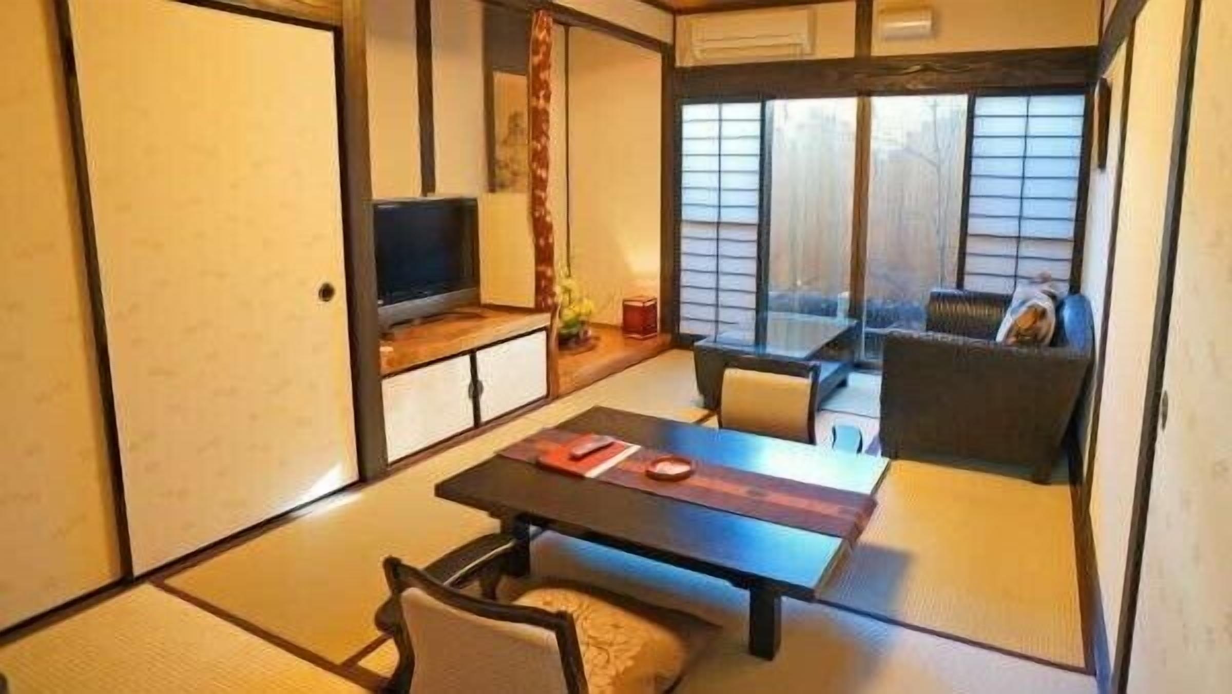 A traditional Japanese-style room with tatami flooring, a low table, a sofa, and a television.