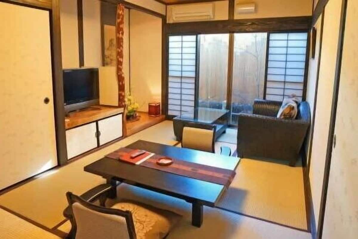 Um quarto tradicional japonês com tatames, uma mesa baixa, um sofá e uma televisão.