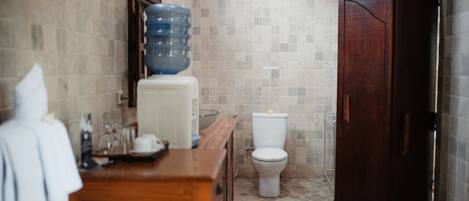 Un baño con tocador de madera, un dispensador grande de agua, un inodoro y una puerta de madera oscura.