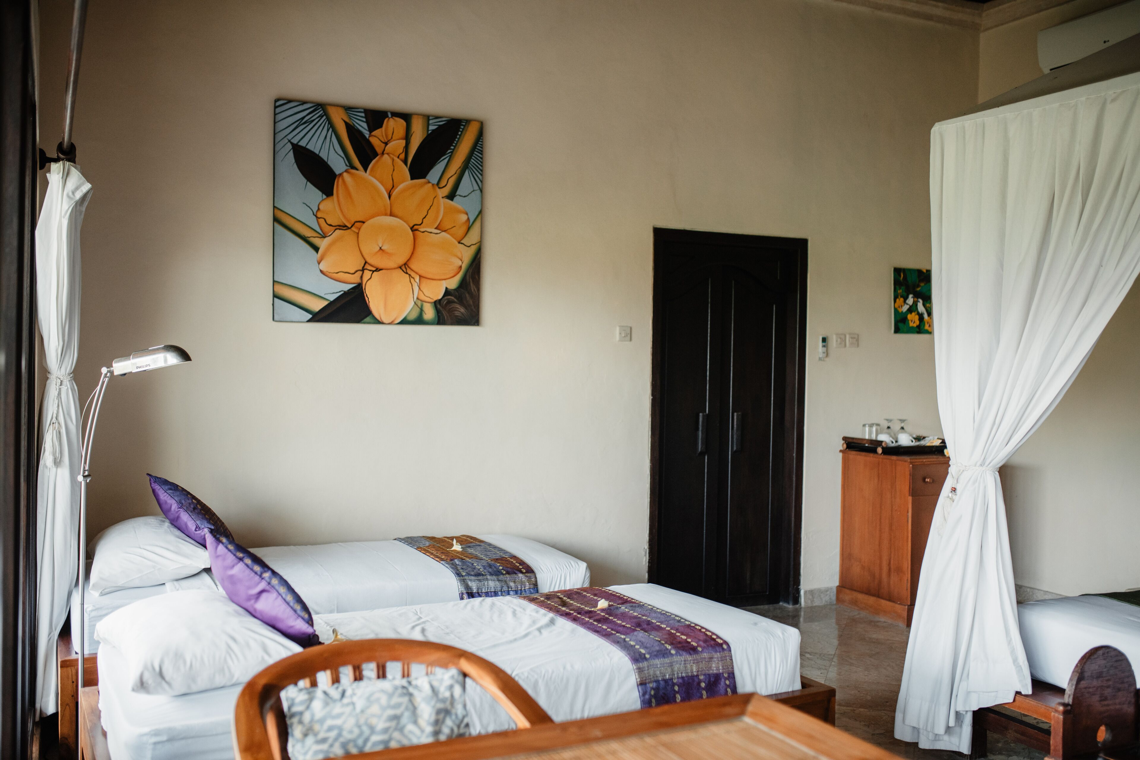 Una habitación con dos camas, una silla de madera, un escritorio, un cuadro de flores, un armario y una cortina.