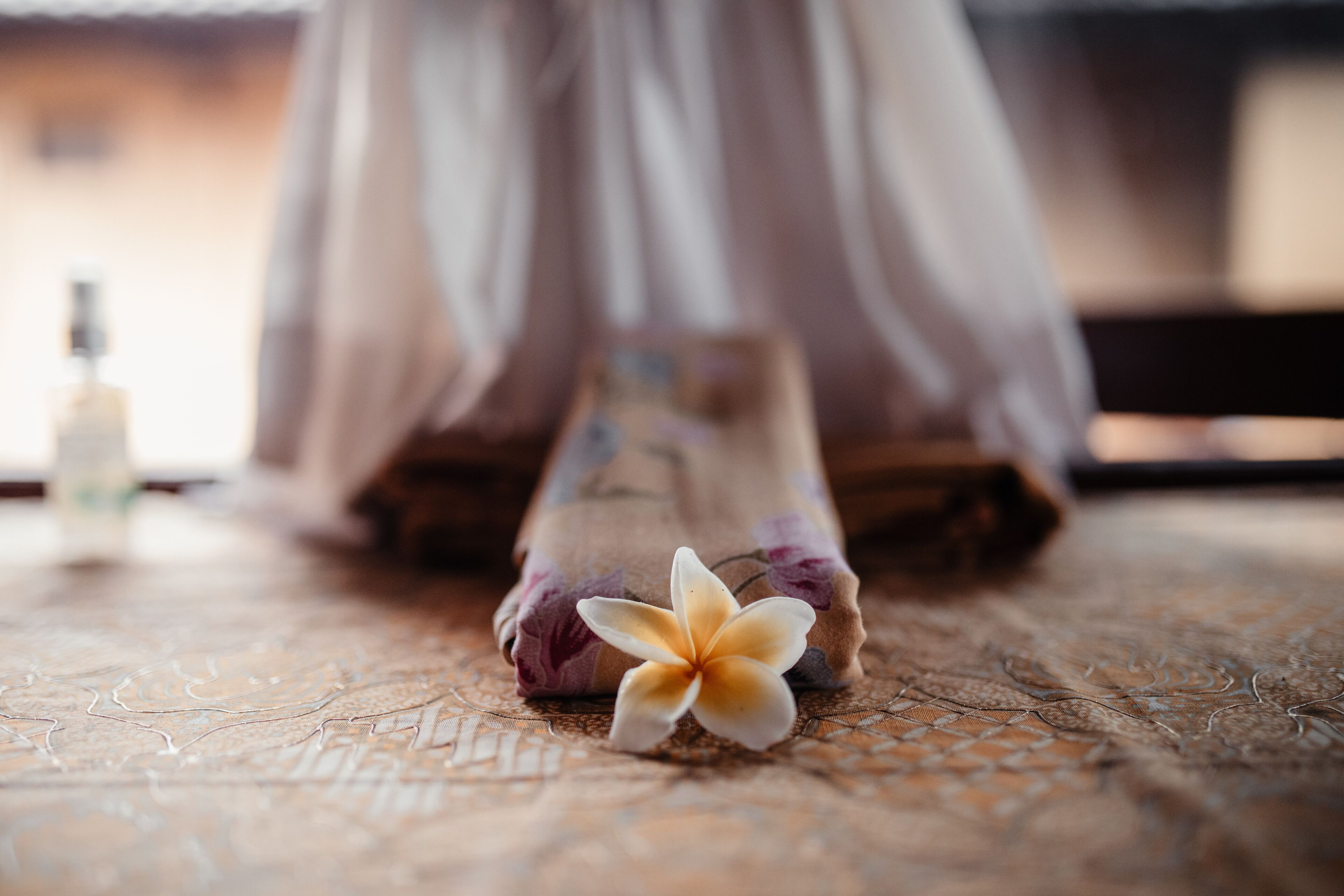A bed with a floral-patterned blanket and a single flower on the bedspread.