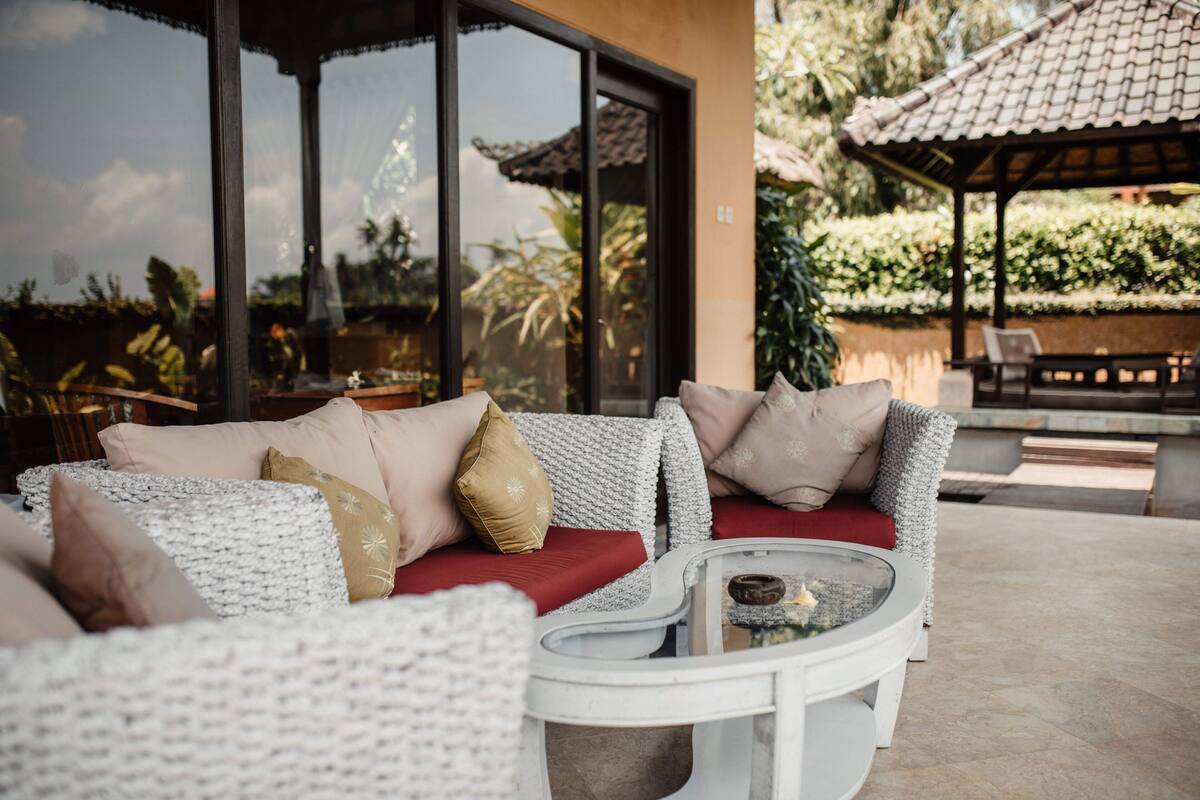 A wicker sofa with red cushions and a glass coffee table in an outdoor setting.
