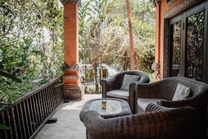 A wicker sofa and table set on a balcony with a view of a garden and a brick wall. - Mandala Desa Boutique Resort (Sukawati)