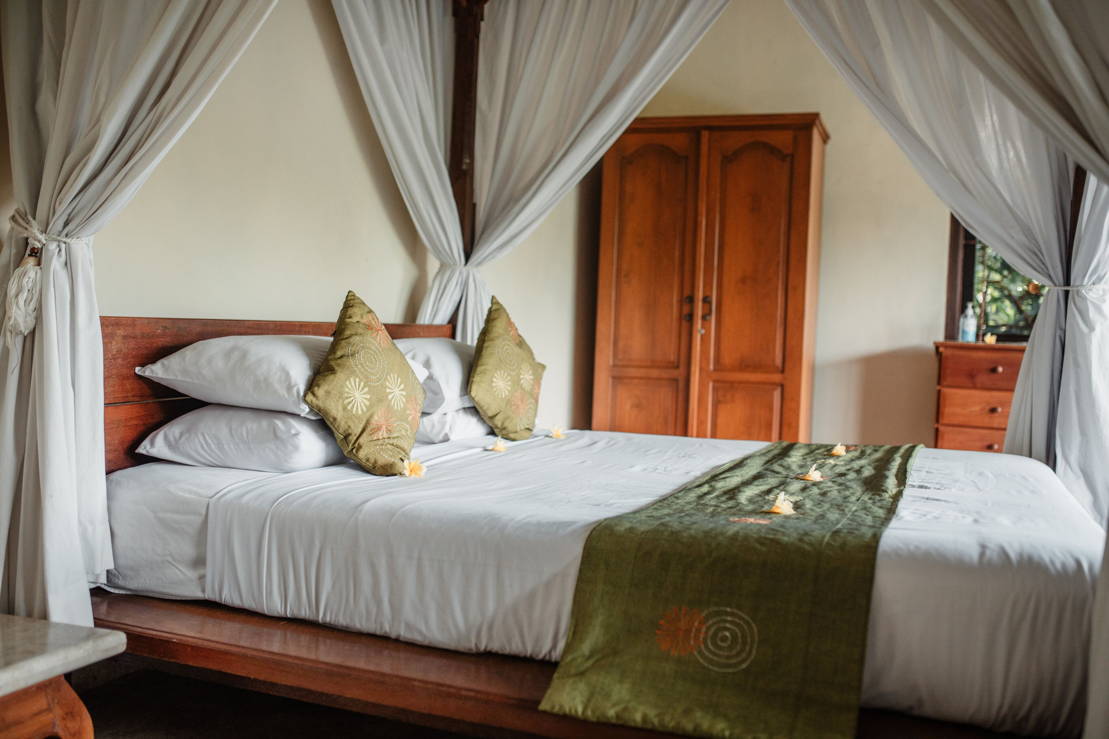 A neatly made bed with white linens and decorative pillows, a wooden headboard, and a green throw blanket.