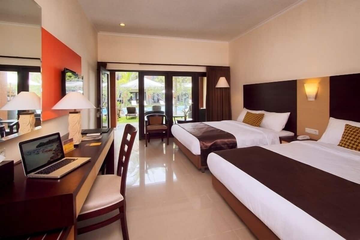 Habitación de hotel con dos camas, un escritorio con una computadora portátil, una silla y vistas al área exterior.