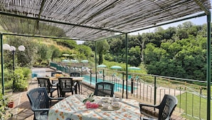 Un patio al aire libre con una mesa lista para comer, rodeada de sillas y vistas a una piscina.