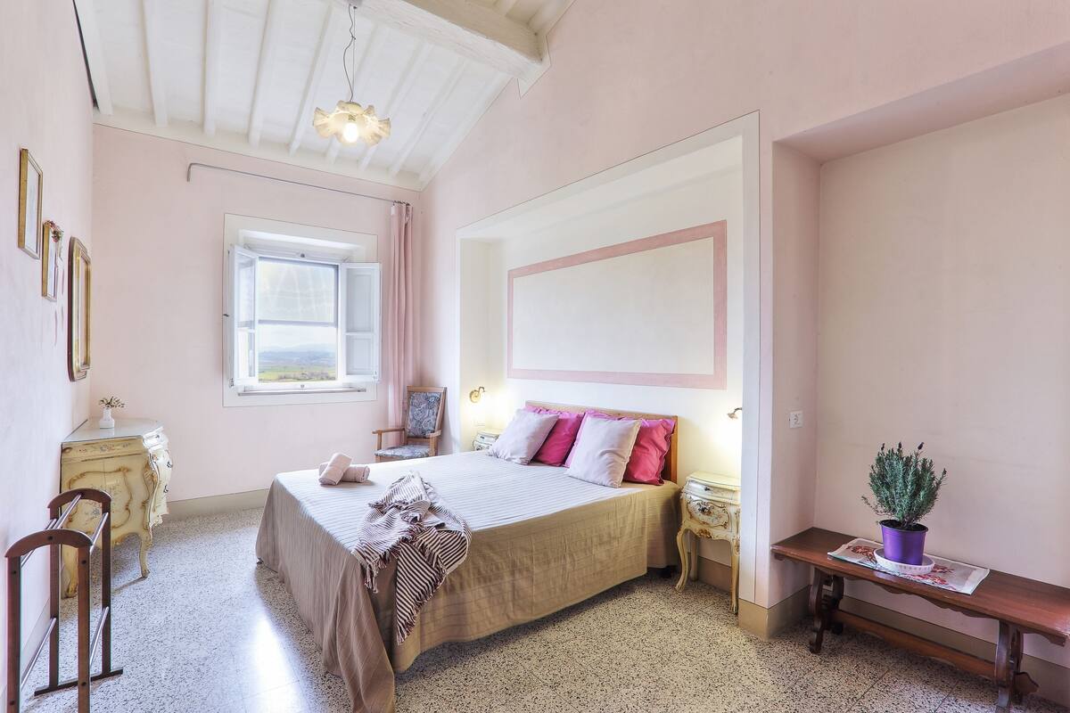 A bedroom with a bed, bedside tables, a dresser, a window, and a potted plant.