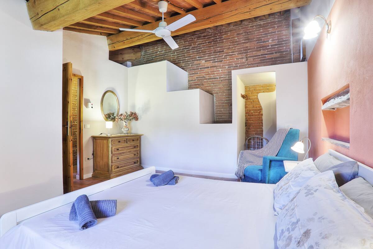 A bedroom with a bed, a dresser, a mirror, a chair, and a staircase.