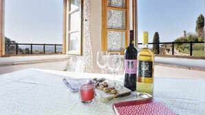 Una mesa con una botella de vino, dos copas, una vela y un libro en un balcón con vistas panorámicas.