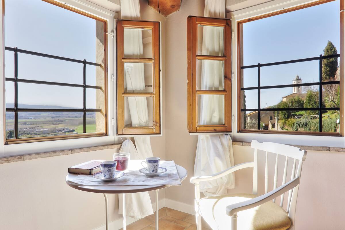A corner room with a table and two chairs, a view of a church, and a book on the table.