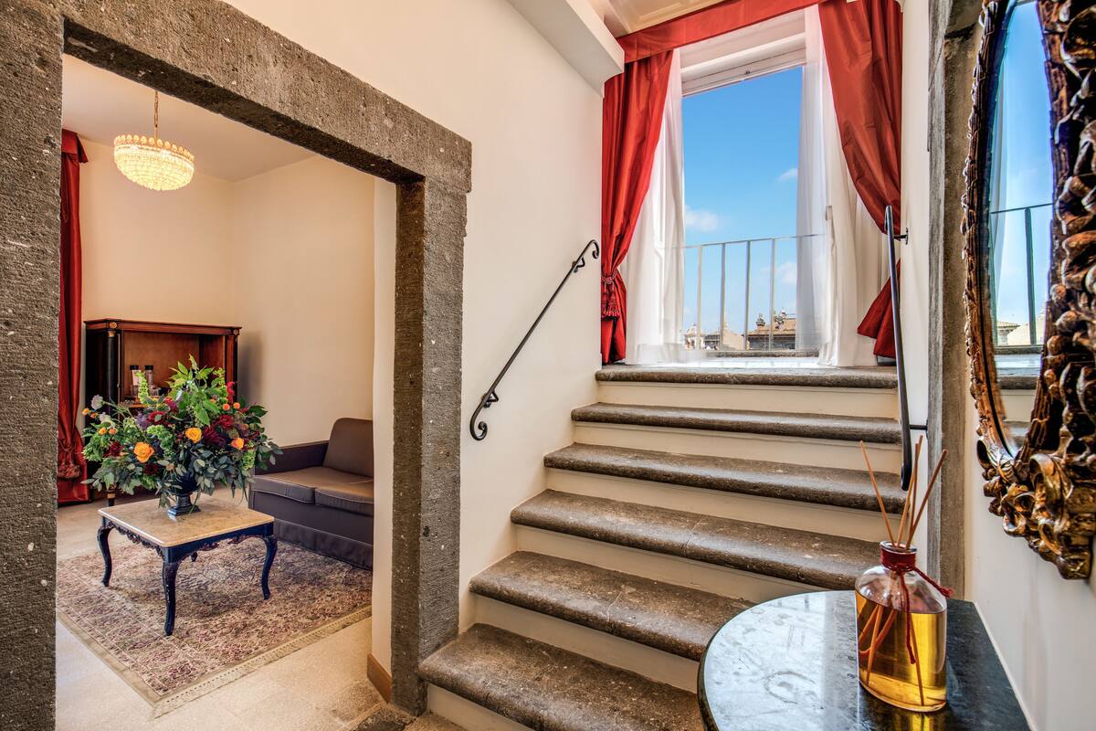 A staircase with stone steps, a wooden table with a vase of flowers, and a red curtain.